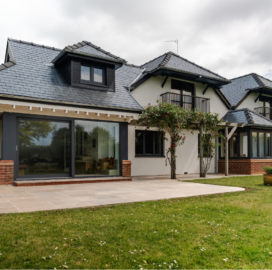 A spacious house featuring a large porcelain patio and expansive lawn, surrounded by greenery.
