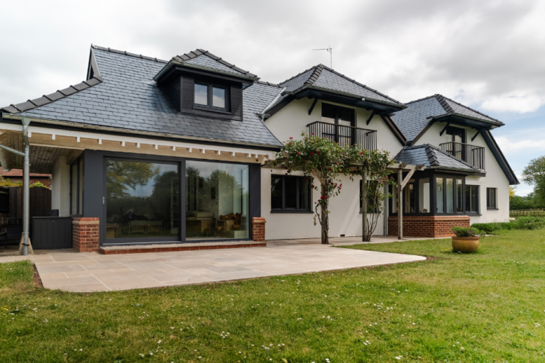 A spacious house featuring a large porcelain patio and expansive lawn, surrounded by greenery.