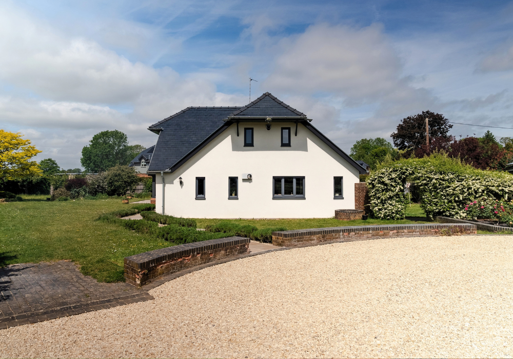 new-gravel-driveway-crowmarsh A large white house is in the middle of the image with a curved driveway with new gravel. A pathway connects the driveway to the house. The sky is blue with some clouds and the garden is full of green plants and a large lawn.