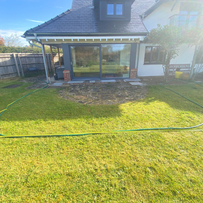 Small rounded patio in front of patio doors with one step down to the patio before new patio renovation. A tape measure and hose have been used to map out the new shape of the patio.