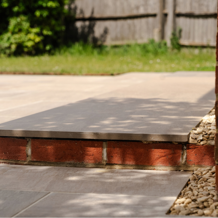 A sturdy brick wall featuring a porcelain step on bricks down to a porcelain patio.